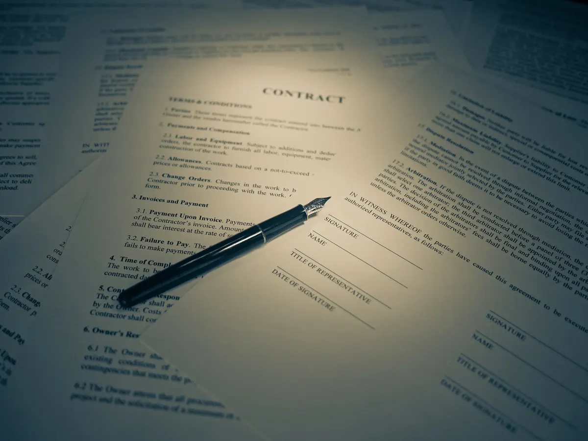 A printed contract with a pen resting on the signature page