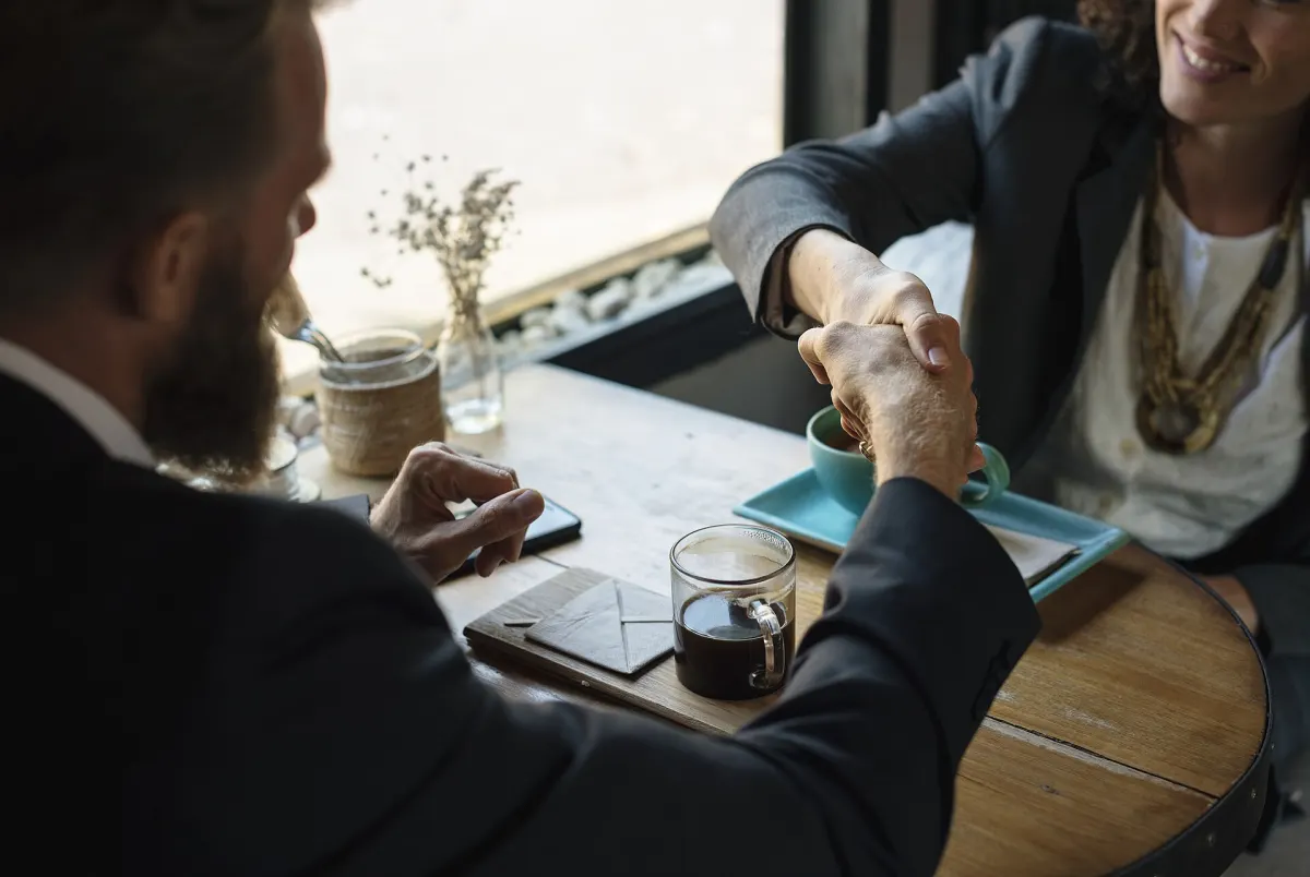 Two people shaking hands across a cafe table
