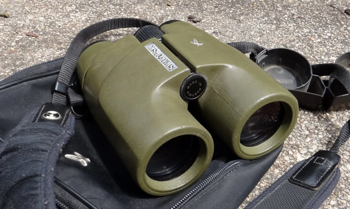 A pair of green binoculars resting on a black carry bag